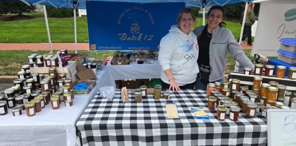 Kristen and a friend at the Batch 12 market booth surrounded by jars of jam, salsa and pickles