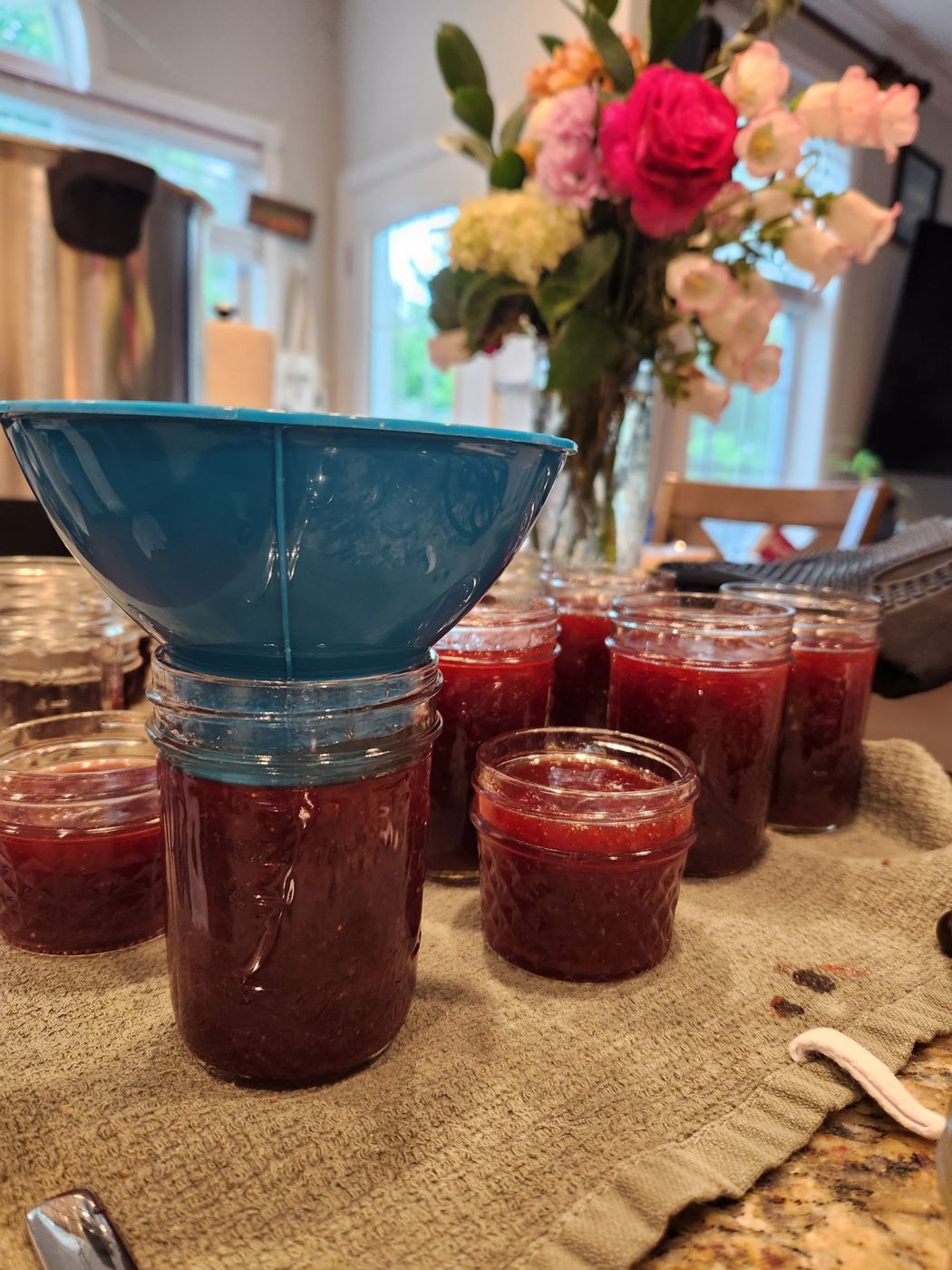 Freshly filled jars of strawberry jam with a blue canning funnel on the kitchen counter